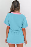 Woman wearing a turquoise outfit with pink trim on a plain background