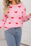 Person wearing a pink sweater with red heart patterns and blue jeans.