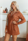 Woman in rust-orange cable-knit zip-up hooded sweater dress by pumpkin-decorated fireplace mantel.
