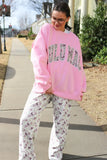 Person wearing a pink sweatshirt with text and patterned pants on a sidewalk.