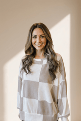 Woman wearing a checkered sweater standing against a neutral background