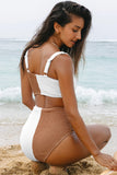 Woman in a two-tone bikini sitting on the beach with ocean waves in the background