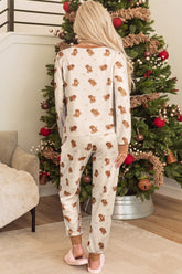 Woman from behind wearing cream teddy bear print pajamas beside a Christmas tree.
