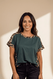 Woman wearing a green top with leopard print sleeves against a beige background