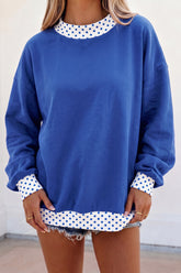 Woman in royal blue sweatshirt with white polka-dot trim and denim shorts.
