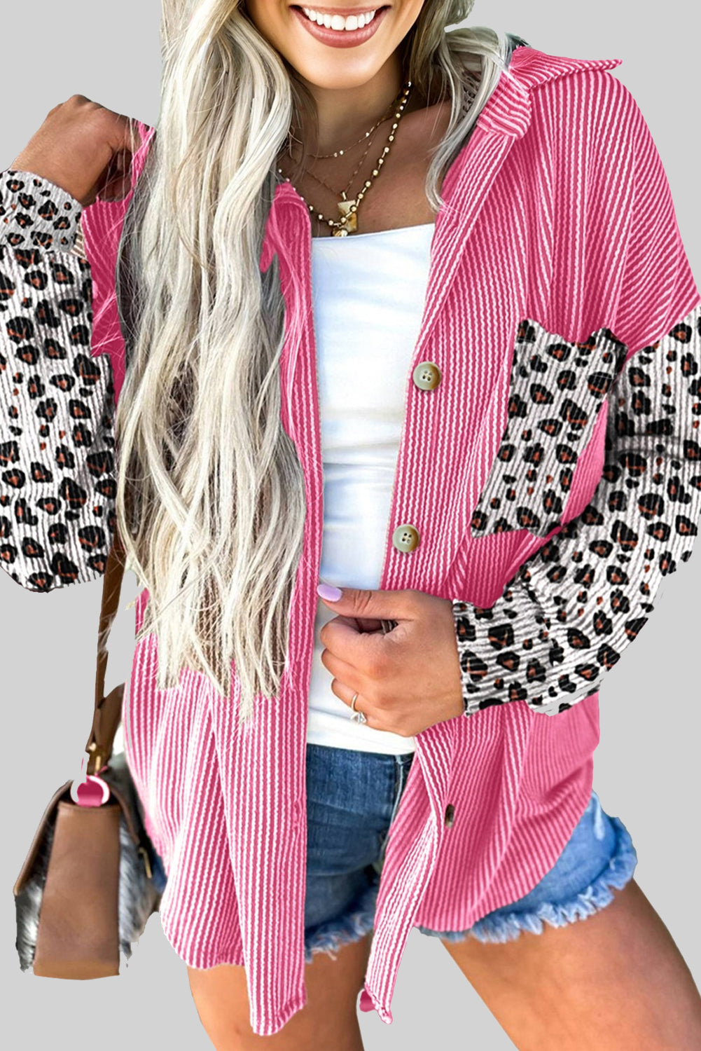 Woman wearing a pink and leopard print jacket with denim shorts on a plain background.