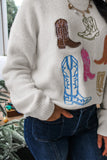 Person in white knit sweater with colorful cowboy boot embroidery and dark blue jeans.