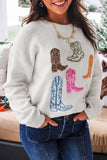 Woman in cream knit sweater with colorful cowboy boot embroidery and dark blue jeans.