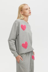 Woman wearing a gray sweatshirt with pink hearts on a white background