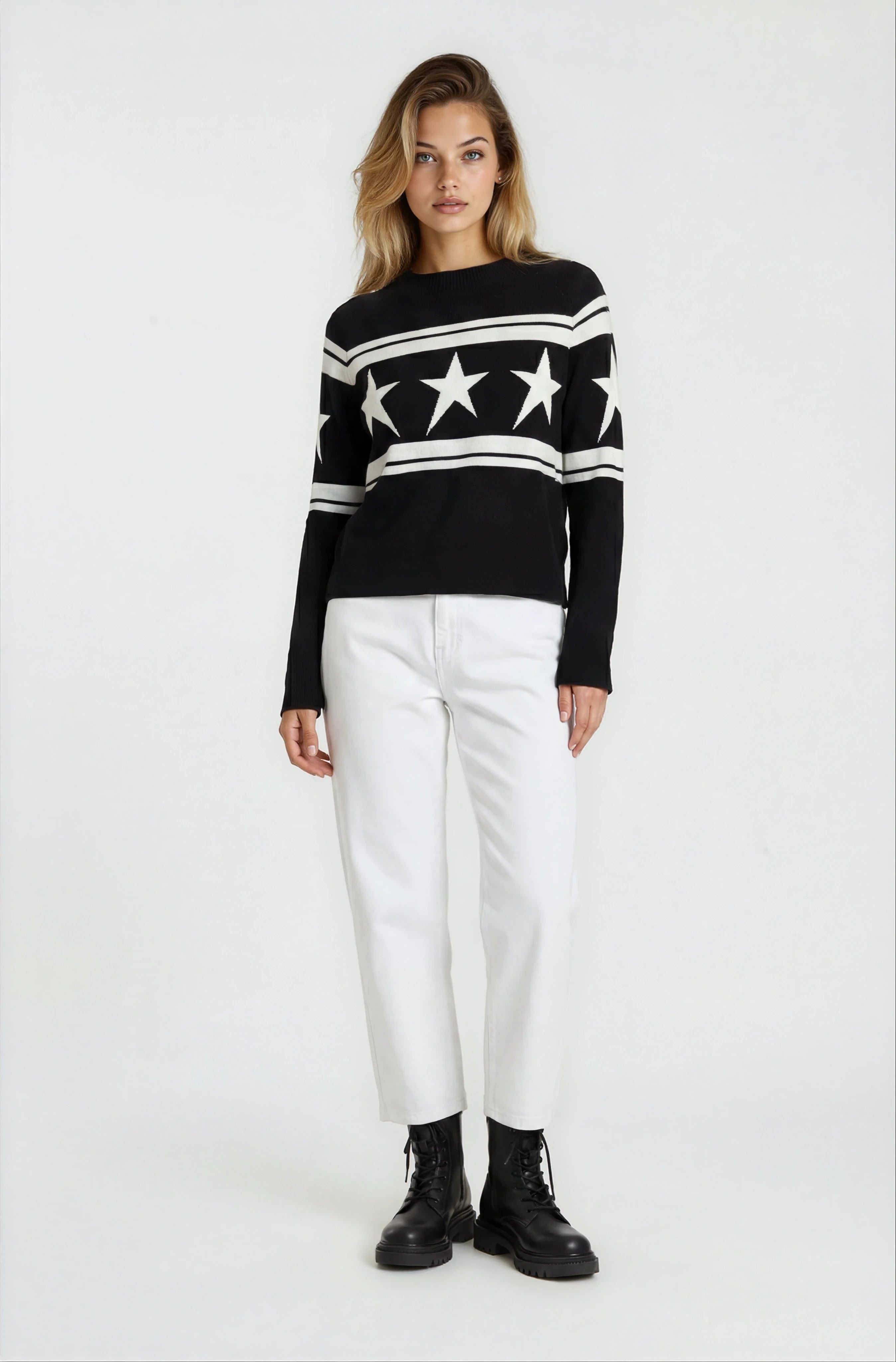 Woman wearing a black sweater with star patterns and white pants on a white background