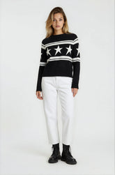 Woman wearing a black sweater with star patterns and white pants on a white background