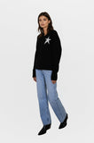 Woman wearing a black sweater with a star design and light blue jeans on a white background
