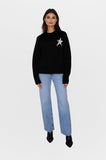 Woman wearing a black sweater with a star design and light blue jeans on a white background