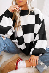 Person wearing a black and white checkered sweater and blue jeans, sitting on a couch.
