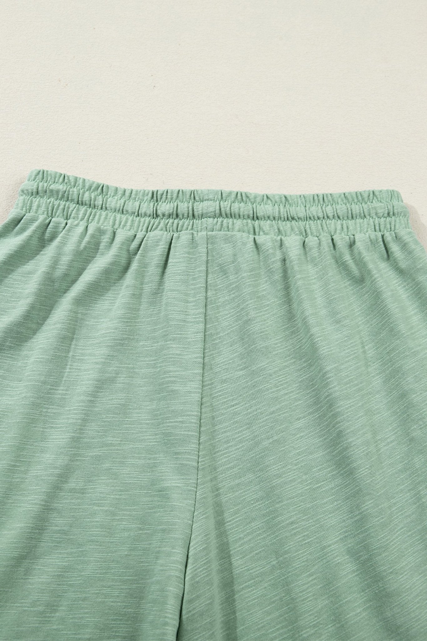 Close-up of green pants with an elastic waistband on a light beige background