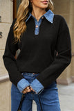 A woman wearing a black knit sweater with a blue denim collar and button placket, paired with blue jeans, photographed outdoors against a beige stone wall.