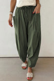 Person wearing olive green wide-leg pants with a white top and sandals on a neutral background