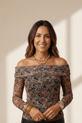 Woman wearing a floral off-shoulder top with gold jewelry against a neutral background