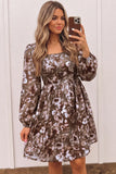 A woman takes a mirror selfie wearing a long-sleeve, knee-length dress with a brown, beige, and white floral pattern. The dress features a square neckline, a fitted waist, and a flared skirt, set against a white paneled wall.