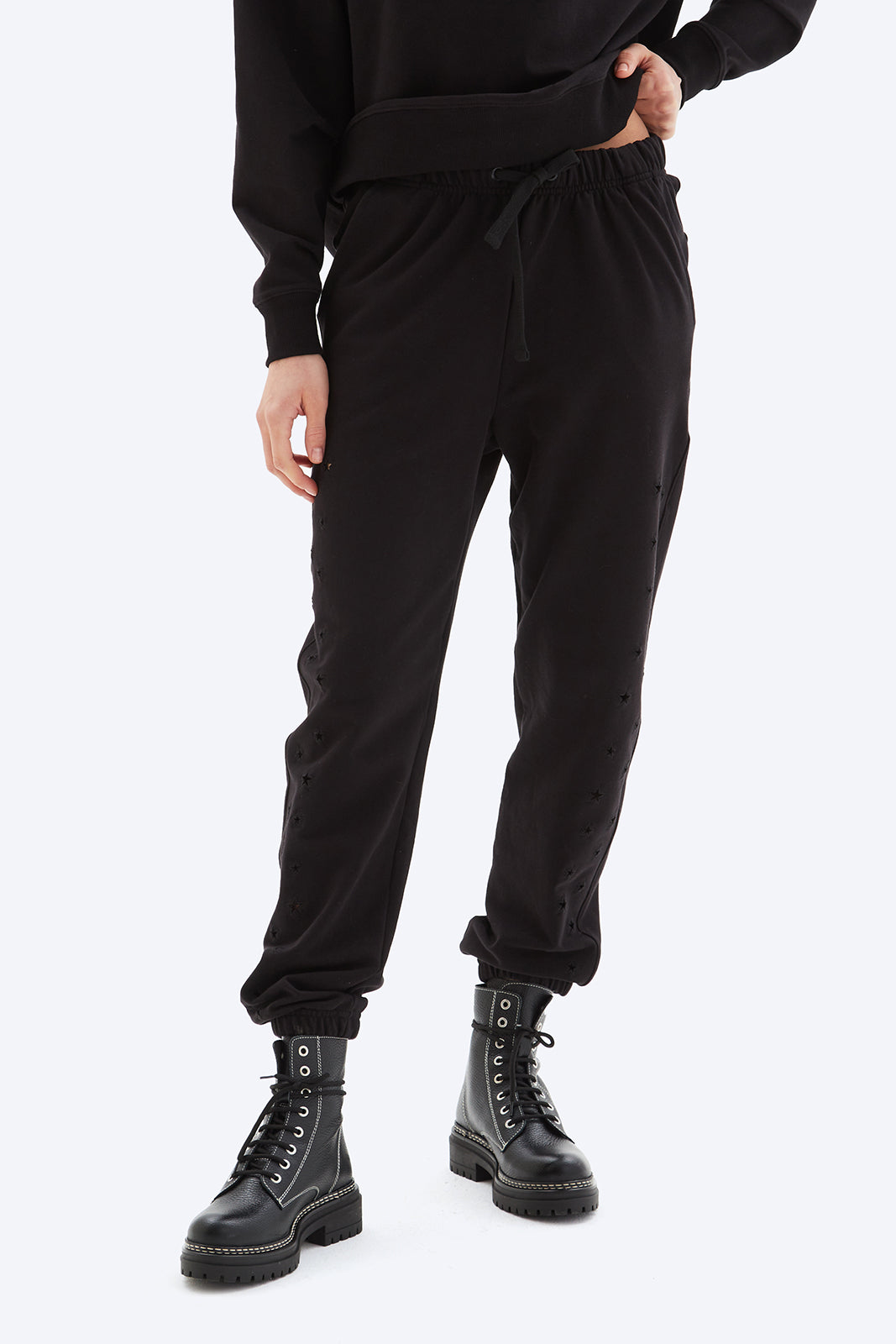 Person wearing black jogger pants and black boots on a white background