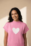 Woman wearing a pink sweater with a white heart design against a beige background