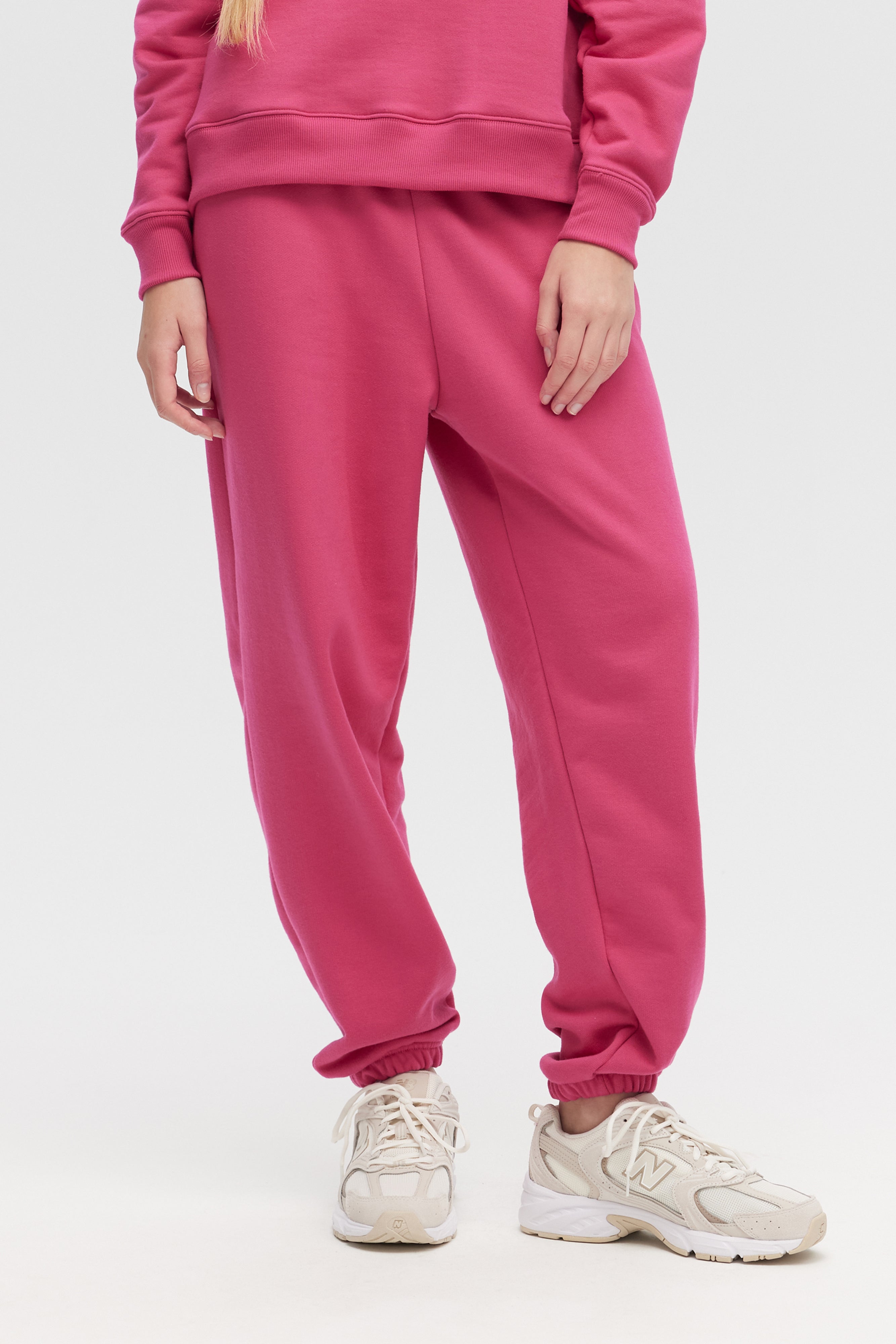 Person wearing a pink tracksuit with white sneakers on a light gray background