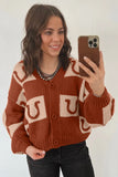 Woman in rust-orange and cream horseshoe cardigan with black jeans and beaded necklace.