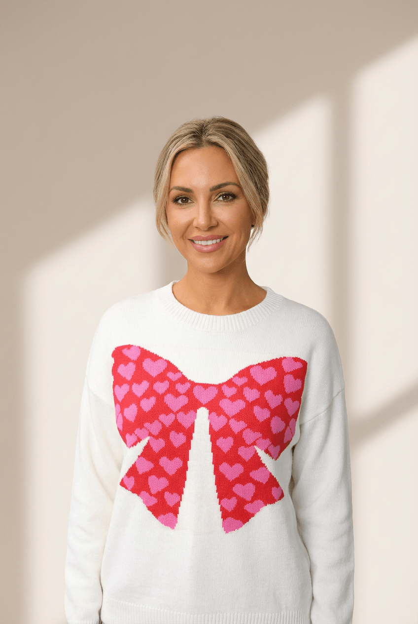 Woman wearing a white sweater with a pink heart bow design on a beige background