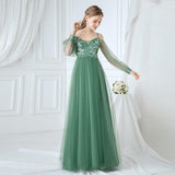 Woman wearing a green evening gown with floral lace details against a white curtain background