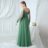 Woman in a green evening gown standing in a room with white curtains and a small table with flowers.