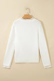 A white long-sleeve knit sweater hanging on a wooden hanger against a warm beige background. The sweater features delicate lace trim detailing at the round neckline and the cuffs.