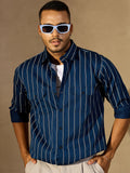 Man wearing a blue pinstripe shirt and sunglasses against a beige background