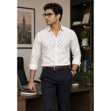 Man in a white patterned shirt and dark pants standing in an office setting.