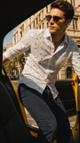 Man in a patterned shirt and sunglasses getting out of a taxi in an urban setting