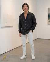 Man wearing a black patterned shirt and white pants in an art gallery setting