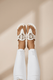 White sandals with gold embellishments worn on a beige background