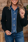 A woman wearing a black ribbed knit cardigan layered over a blue denim button-up shirt, paired with blue jeans, set against a rustic wooden wall background.