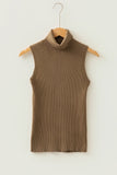 A sleeveless ribbed knit turtleneck sweater vest in a warm taupe-brown color, hanging on a wooden hanger against a plain off-white wall.