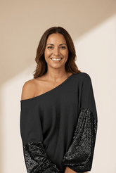 Woman wearing a black off-shoulder top with sequin sleeves on a beige background