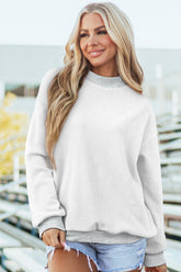 Woman wearing a light gray sweatshirt and denim shorts with a blurred outdoor background