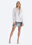 Woman wearing a white blazer and silver sequin skirt on a white background