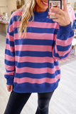 A woman takes a mirror selfie wearing an oversized long-sleeve sweatshirt with horizontal pink and navy blue stripes, paired with black pants in a retail store setting.