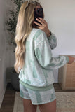 A woman takes a mirror selfie wearing a matching sage green and white patchwork lounge set consisting of a long-sleeve sweatshirt and shorts.