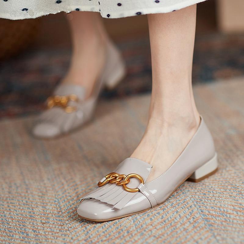 Light gray loafers with gold chain detail worn by a person on a textured rug.