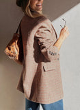 Woman wearing a plaid coat holding a brown leather bag against a neutral background