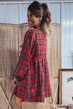A woman wearing a red tartan plaid long-sleeve dress, standing in front of a wooden folding screen.