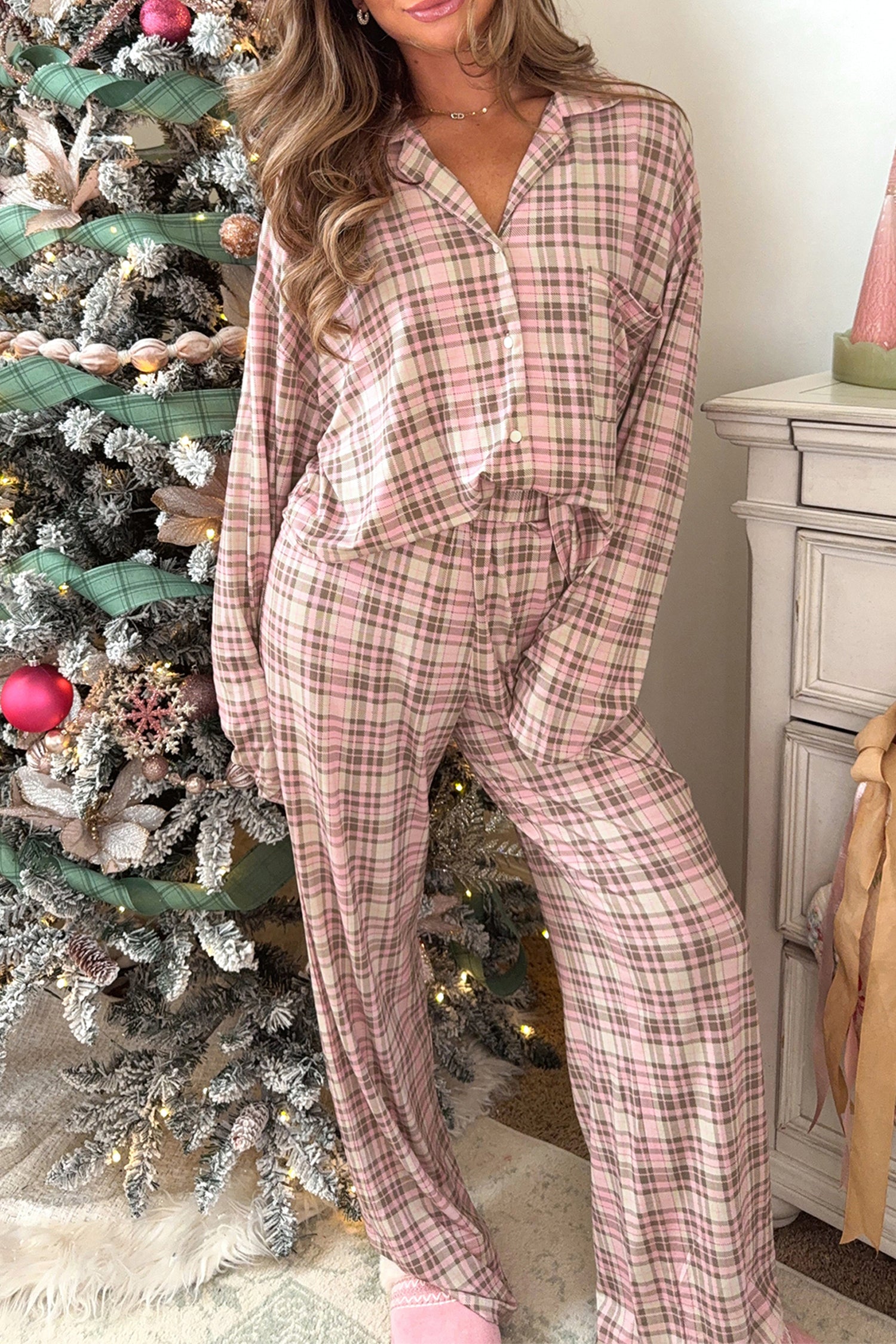 Woman wearing pink and beige plaid Christmas pajamas by a tree.