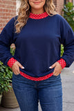 A woman wearing a navy blue crewneck sweatshirt with red and white polka dot trim on the collar, cuffs, and hem, paired with blue jeans.