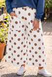 White wide-leg pants with large brown polka dots, featuring side pockets and a drawstring waist, shown on a model wearing a blue sweatshirt and white sneakers.