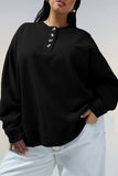 Woman wearing an oversized black henley sweatshirt with gold-tone buttons and white pants.